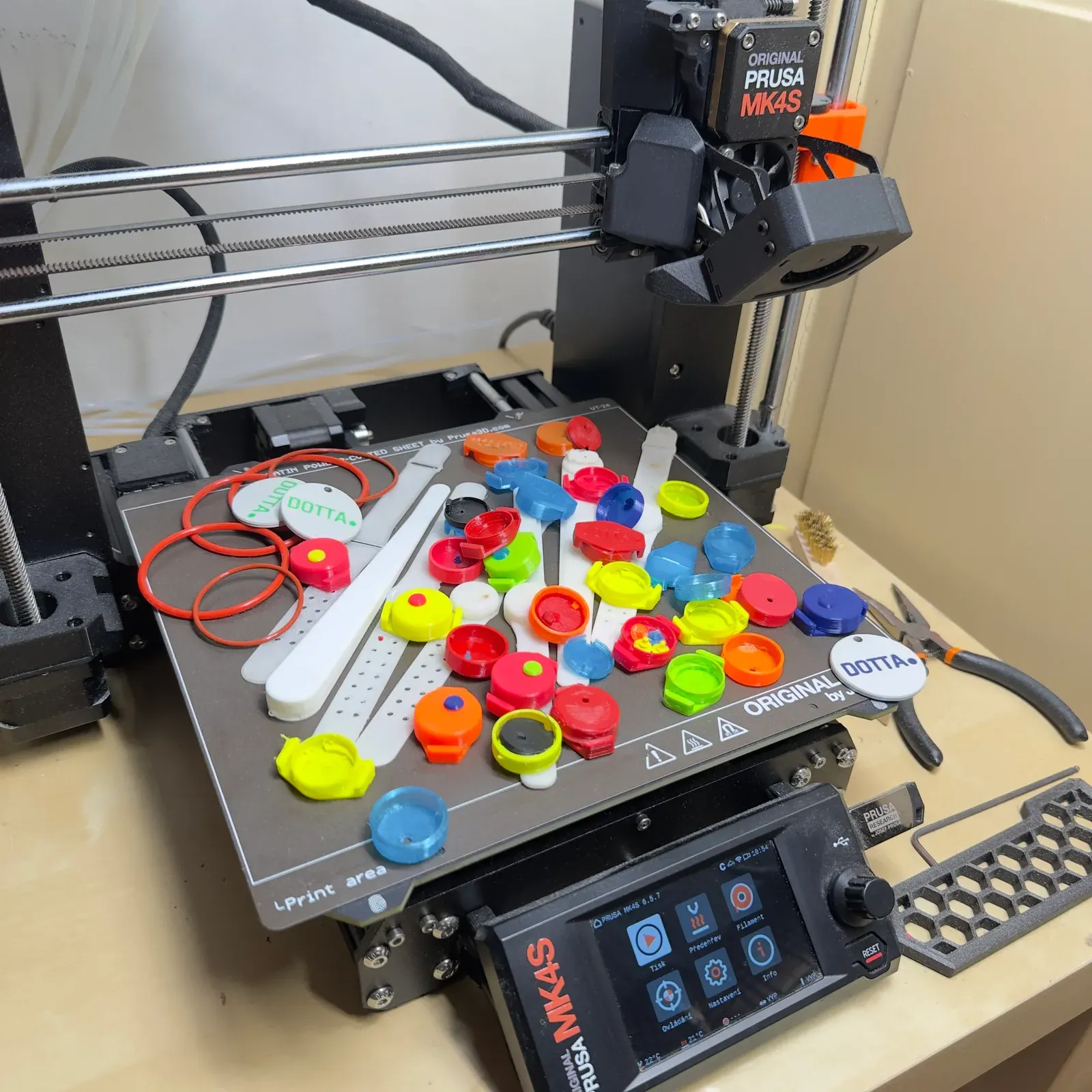 Rozdělaná 3D tiskárna s barevnými prototypy ovladačů a O-kroužky